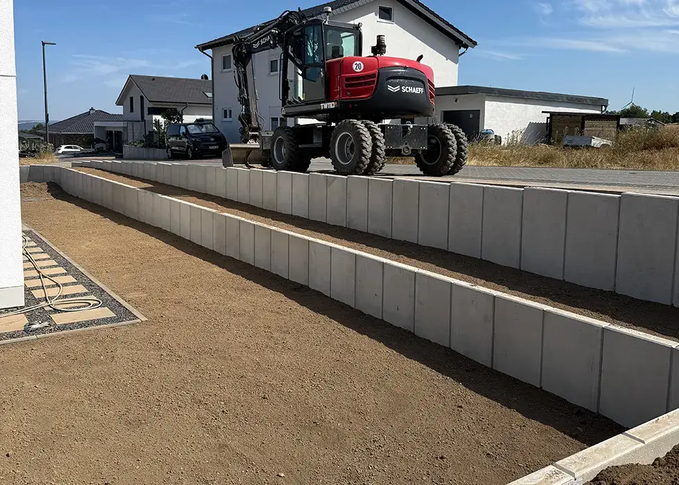 Baugrundstück mit Stützwänden Baugrundstück mit gestuften Stützwänden aus Beton und einem kleinen Bagger auf der obersten Stufe vor Wohnhäusern