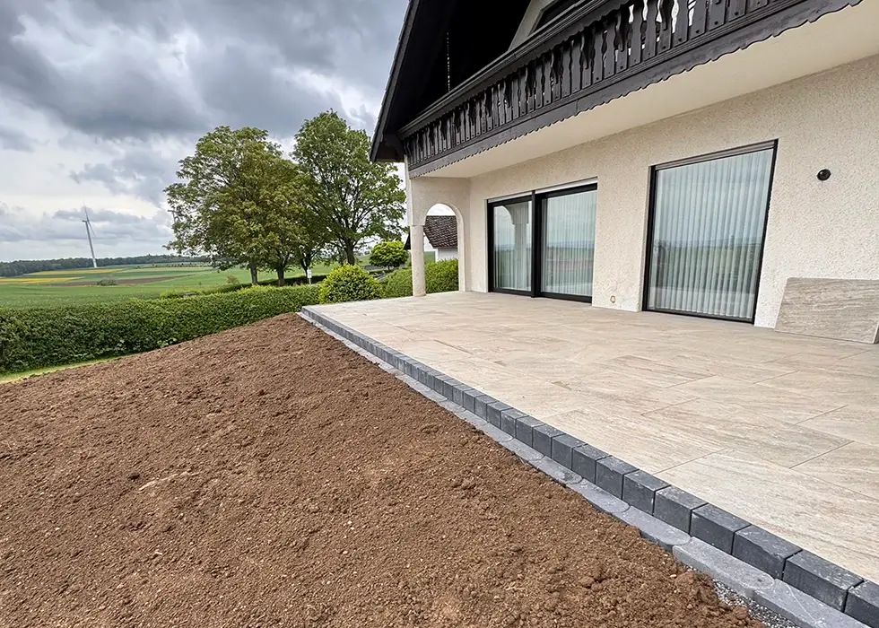 Haus mit großer Terrasse Haus mit großer Terrasse und frisch aufgeschüttetem Erdhang davor unter bewölktem Himmel