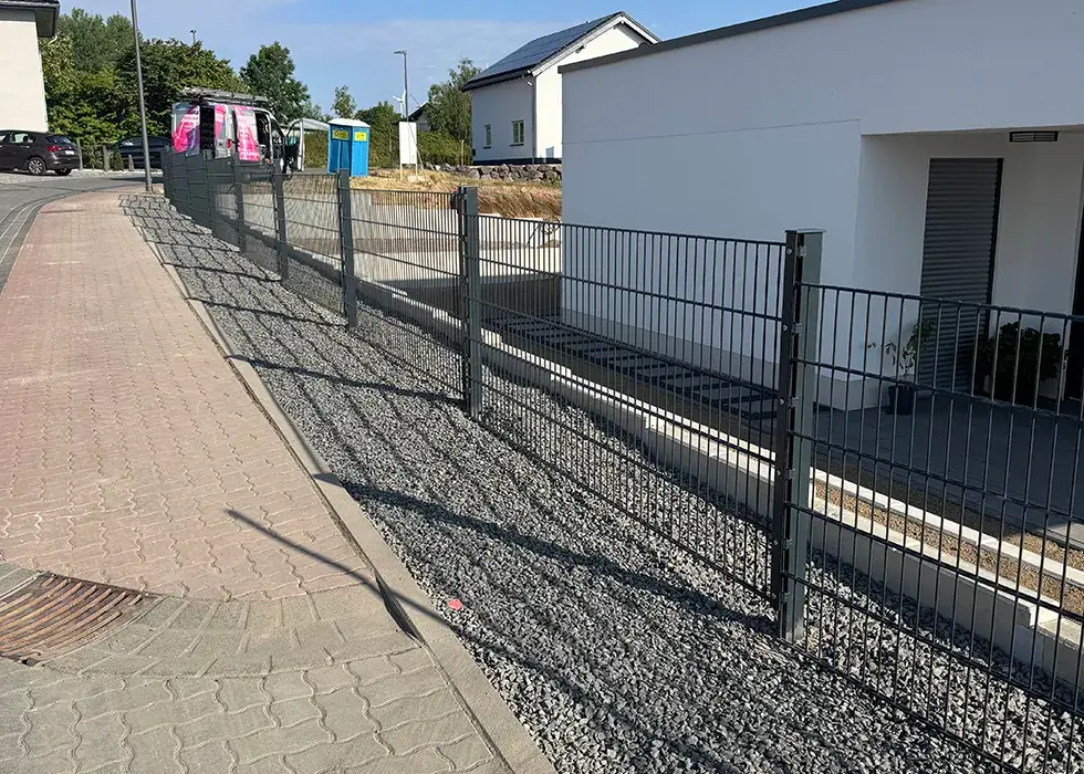 Zaunanlagen Metallzaun mit senkrechten und waagerechten Stäben entlang eines Gehwegs und eines Hauses